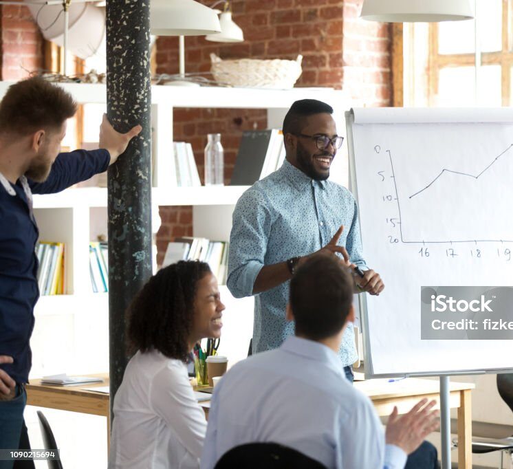 Smiling black leader giving presentation at business seminar, friendly african american mentor speaking at diverse team office training, happy coach talking laughing having fun at group meeting